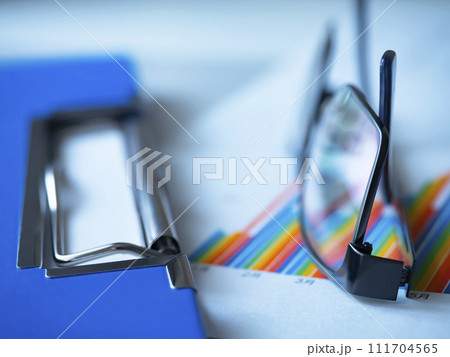 テーブルに置かれたグラフとバインダーとメガネ 111704565