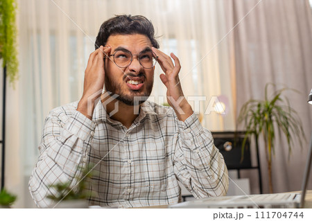Tired ill Indian businessman suffering from headache problem tension migraine stress at home office Tired ill Indian businessman suffering from headache problem tension migraine stress at home office 111704744