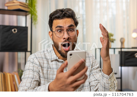 Happy amazed Indian man working on smartphone shocked by sudden victory game lottery online winning 111704763