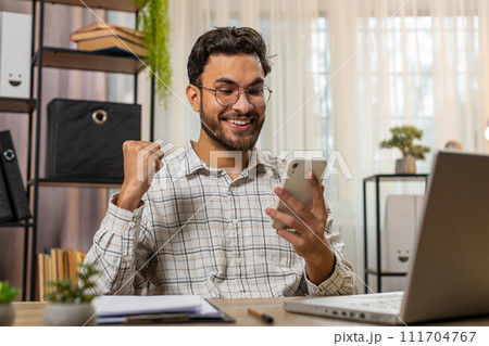 Happy Indian businessman using smartphone celebrating success victory winning lottery casino jackpot Happy Indian businessman using smartphone celebrating success victory winning lottery casino jackpot 111704767