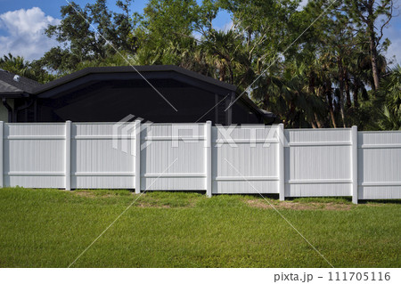 White vinyl picket fence on green lawn surrounding property grounds for backyard protection and privacy 111705116