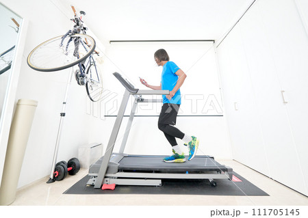 スマホを見ながらランニングマシンで走る中年男性 スマホを見ながらランニングマシンで走る中年男性 111705145
