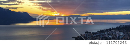 Scenic view of sunset over the Leman lake with yellow sky with clouds and Alps mountains in background, Montreux, Switzerland. Scenic view of sunset over the Leman lake with yellow sky with clouds and Alps mountains in background, Montreux, Switzerland. 111705248