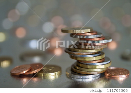 Pile of shiny coins different sizes and colors stacked unevenly on each other on colorful blurred blue abstract background. Money saving and financial risk concept. Pile of shiny coins different sizes and colors stacked unevenly on each other on colorful blurred blue abstract background. Money saving and financial risk concept. 111705306