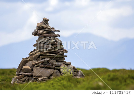 Lit by bright summer sun uneven mountain stones stacked and balanced like pyramid pile on green grassy valley on light white blue copy space sky background. Tourism. Traveling and landmark concept. 111705417
