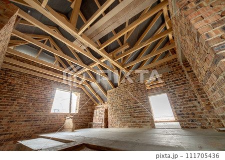 Interior of unfinished brick house with concrete floor, bare walls ready for plastering and wooden roofing frame attic under construction. Interior of unfinished brick house with concrete floor, bare walls ready for plastering and wooden roofing frame attic under construction. 111705436