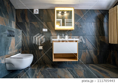 Interior of modern stylish bathroom with black tiled walls, curtain shower place and wooden furniture with wash basin and big illuminated mirror. 111705443