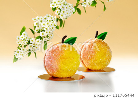 Sugared peach-shaped pastries on warm backdrop with blooming tree 111705444