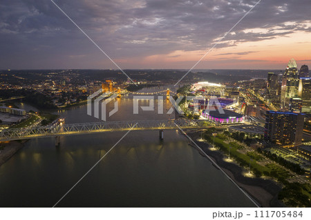 Highway traffic with driving cars on bridge in downtown district of Cincinnati city in Ohio, USA. American city skyline with brightly illuminated high commercial buildings at night Highway traffic with driving cars on bridge in downtown district of Cincinnati city in Ohio, USA. American city skyline with brightly illuminated high commercial buildings at night 111705484