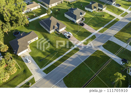 Aerial view of street traffic with driving cars in small town. American suburban landscape with private homes between green palm trees in Florida quiet residential area Aerial view of street traffic with driving cars in small town. American suburban landscape with private homes between green palm trees in Florida quiet residential area 111705910