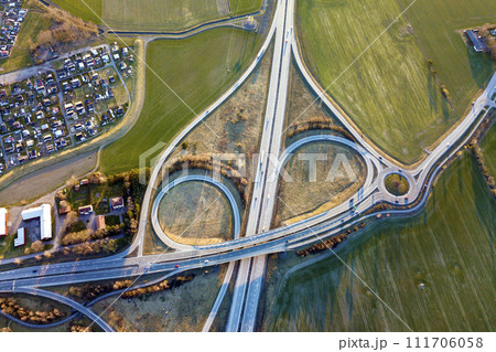 Aerial top view of modern highway road intersection, house roofs on spring green field background. Drone photography. Aerial top view of modern highway road intersection, house roofs on spring green field background. Drone photography. 111706058
