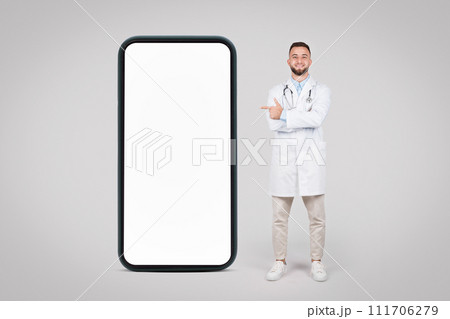 Happy doc with arms crossed posing big phone and pointing at blank screen, mockup 111706279
