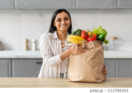 Cheerful young indian woman with paper bag full of grocery Cheerful young indian woman with paper bag full of grocery 111706301