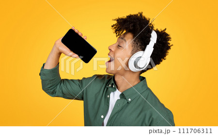 Joyful young black guy singing karaoke on yellow background 111706311