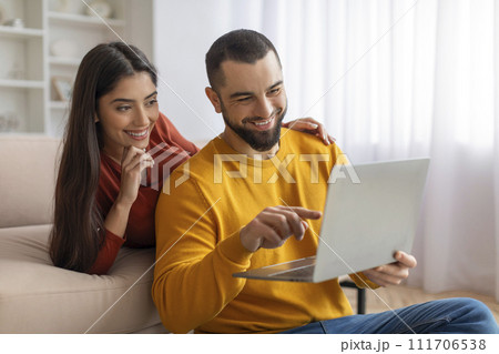Happy young couple websurfing on laptop together while relaxing at home 111706538