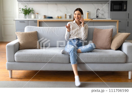 Cheerful young woman chatting on cellphone, sitting on sofa 111706590