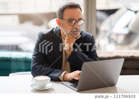 Mature professional contemplating work on laptop in a café Mature professional contemplating work on laptop in a café 111706928