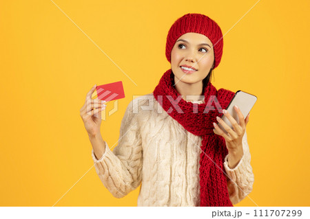 Lady with phone and credit card shops online, yellow backdrop 111707299
