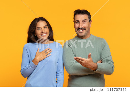 Smiling caucasian old woman holds her hand on chest in gratitude as man gestures openly towards Smiling caucasian old woman holds her hand on chest in gratitude as man gestures openly towards 111707553