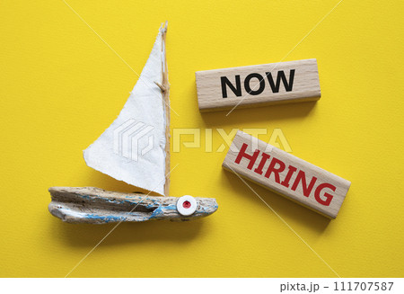Now Hiring symbol. Concept word Now Hiring on wooden blocks. Beautiful yellow background with boat. Business and Now Hiring concept. Copy space Now Hiring symbol. Concept word Now Hiring on wooden blocks. Beautiful yellow background with boat. Business and Now Hiring concept. Copy space 111707587