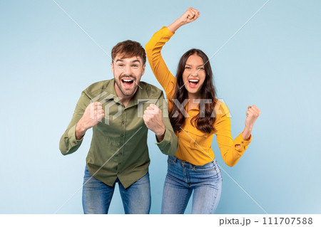 Ecstatic couple celebrating success with fists raised, blue background 111707588