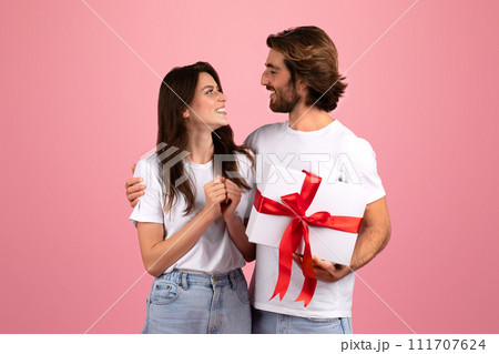 Affectionate couple sharing a joyful moment, with a man holding a large white gift 111707624