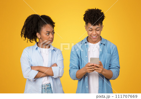 An African American woman skeptically looks at a young man who is happily engrossed in his smartphone 111707669
