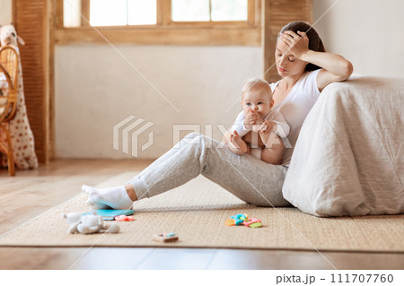 Depressed young woman sitting with cute baby boy on floor Depressed young woman sitting with cute baby boy on floor 111707760