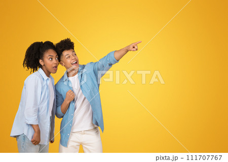 Excited African American young man pointing away with a thrilled expression as the young woman 111707767