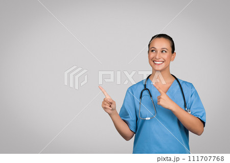 Glad european lady doctor point fingers to copy space, isolated on gray background, place for ad 111707768