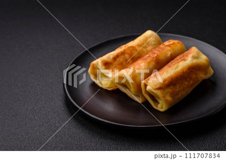 Delicious fried pancakes with filling rolled on a dark concrete background 111707834