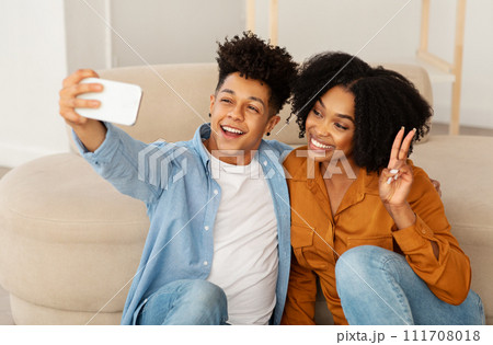 A cheerful young couple captures a joyful moment with a selfie, the man in a denim shirt flashing a bright smile 111708018