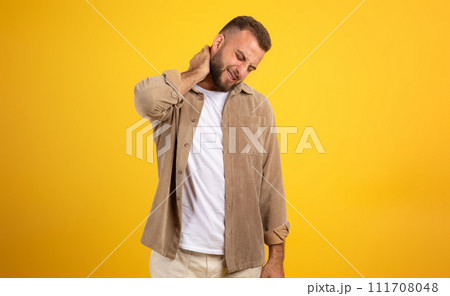 Unhappy millennial european man with beard in casual massaging neck with hand, suffer from pain 111708048