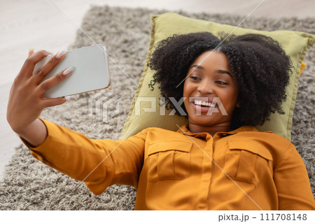 A joyful African American woman with a vivacious smile lies on a pillow 111708148