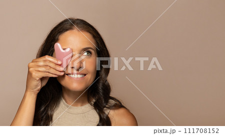 Smiling european senior woman put quartz petal to eye, enjoy natural beauty care massage 111708152