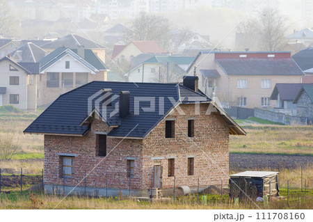Brand new spacious brick two story residential house with tiling roof and windows openings in suburban neighborhood on background of distant city.Building, mortgage and rel estate property. 111708160