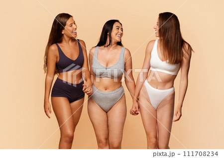 Three diverse young women in underwear holding hands and laughing together Three diverse young women in underwear holding hands and laughing together 111708234