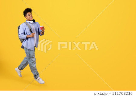 Happy male student walking with coffee on yellow background 111708236