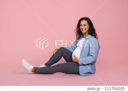Happy pregnant young woman sitting on floor on pink 111708283