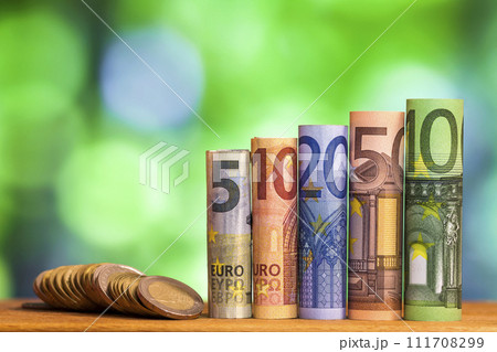 Five, ten, twenty, fifty and one hundred euro rolled bills banknotes, with euro coins on green blurred bokeh background. Five, ten, twenty, fifty and one hundred euro rolled bills banknotes, with euro coins on green blurred bokeh background. 111708299