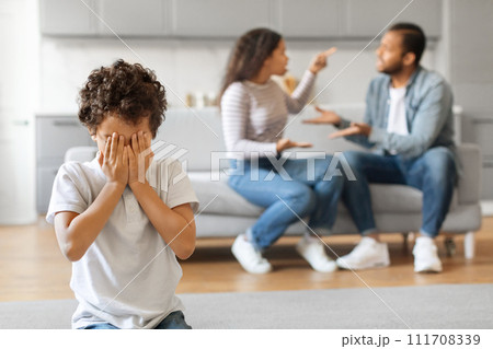Upset black preteen boy covering face with hands while his parents arguing Upset black preteen boy covering face with hands while his parents arguing 111708339