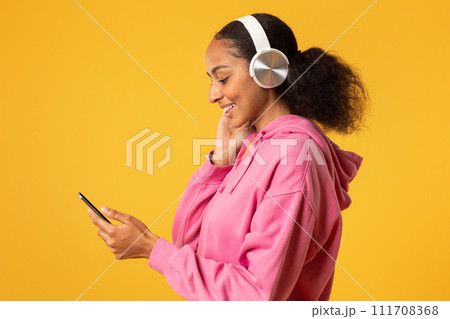Black Girl In Headphones Using Cellphone Over Yellow Studio Background Black Girl In Headphones Using Cellphone Over Yellow Studio Background 111708368