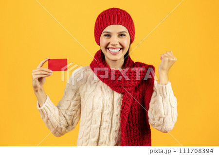 Young woman holding credit card shaking fist on yellow background 111708394