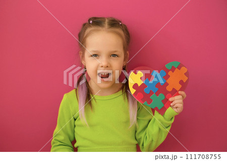 A girl talks about autism by showing a heart-shaped postcard decorated with multicolored puzzles A girl talks about autism by showing a heart-shaped postcard decorated with multicolored puzzles 111708755
