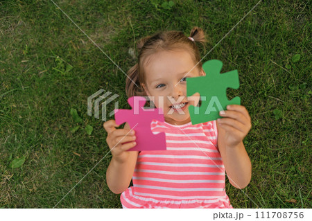 The child holds two large pieces in the shape of a puzzle lying on the grass. Intellectual development and acquisition of non-standard thinking skills The child holds two large pieces in the shape of a puzzle lying on the grass. Intellectual development and acquisition of non-standard thinking skills 111708756
