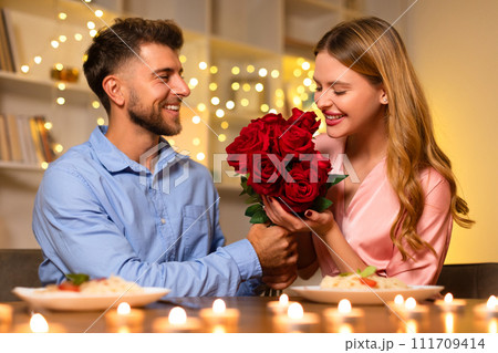 Man giving woman a bouquet of roses during a romantic dinner Man giving woman a bouquet of roses during a romantic dinner 111709414