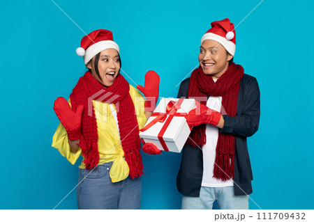 Glad millennial asian guy in hat gives box present to surprised woman 111709432