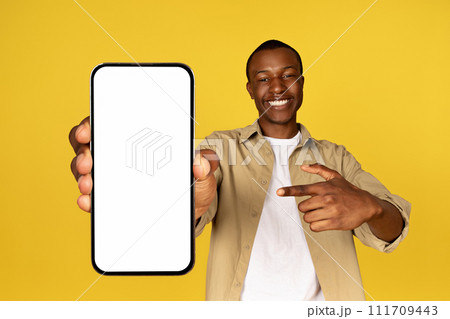 Cheerful young black guy in casual pointing finger at mobile smartphone with empty screen Cheerful young black guy in casual pointing finger at mobile smartphone with empty screen 111709443