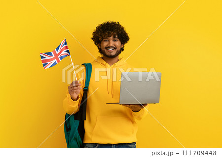 Happy young indian guy holding laptop and flag of UK Happy young indian guy holding laptop and flag of UK 111709448