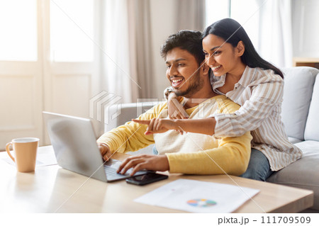 Happy young indian couple websurfing on laptop together at home Happy young indian couple websurfing on laptop together at home 111709509